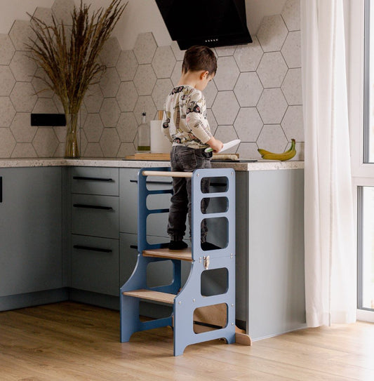 Ein Junge steht im multifunktionalen 2-in-1 Lernturm & Kindertisch in skandinavischem Design in der Farbe blau, Hersteller: Duck Woodworks