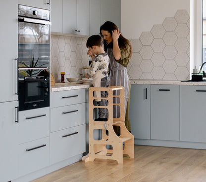 Eine Junge steht im multifunktionalen 2-in-1 Lernturm & Kindertisch in skandinavischem Design in der Farbe natur, Hersteller: Duck Woodworks