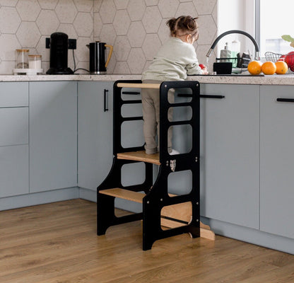 Kleines Mädchen steht im multifunktionalen 2-in-1 Lernturm & Kindertisch in skandinavischem Design in der Farbe schwarz, Hersteller: Duck Woodworks