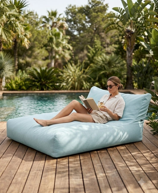 Lesende Frau mit Sonnenbrille liegt auf dem Outdoor-Sitzsack SUNBED SOFA von Slowdown, Bild: KI-generiert 