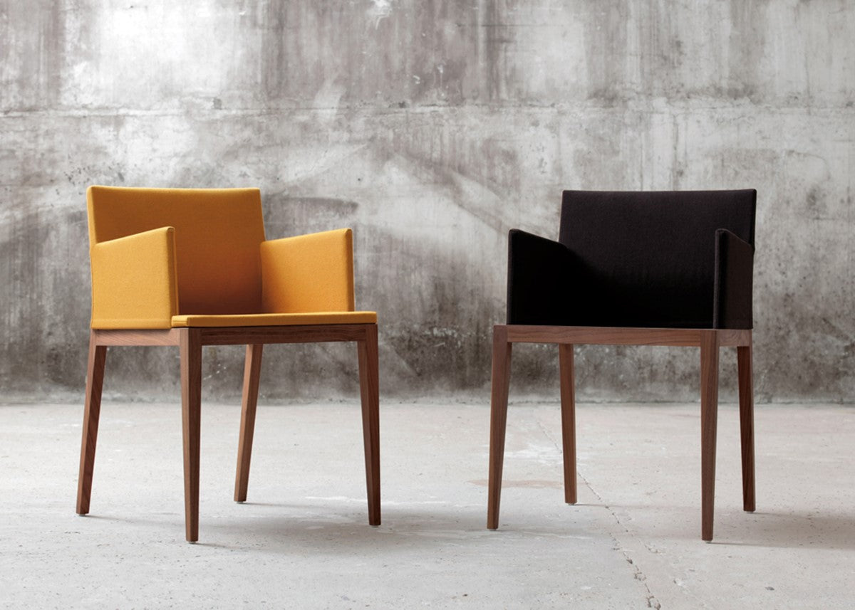Zwei Stühle BLOOM Nussbaum mit gelben und schwarzem Bezug von Mint Furniture vor einer grauen Betonwand