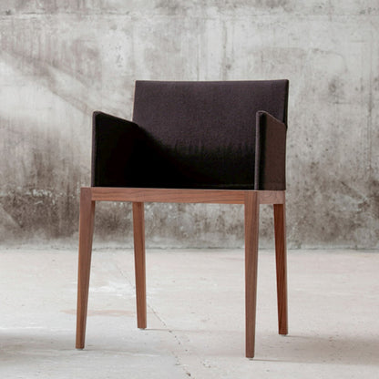 Stuhl BLOOM Nussbaum mit schwarzem Bezug von Mint Furniture vor einer Betonwand