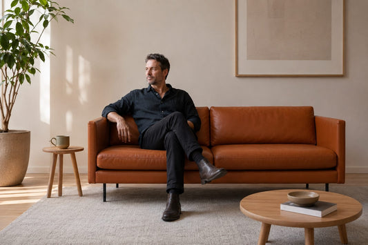 Ledersofa LEAF in Cognac in skandinavischem Design, auf dem ein schwarz gekleideter, entspannter Mann sitzt; Hersteller: Möbelstudio Oot-Oot, Bild: KI-generiert