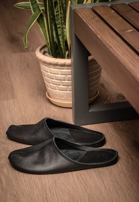 Sulbi Slippers aus schwarzem Leder der  estnischen Firma OmaKing stehen vor einer Garderobenbank