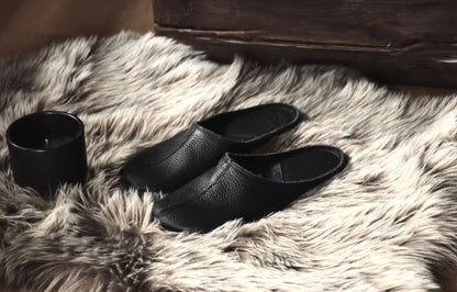 Sulbi Slippers aus schwarzem Leder auf einnem Fellteppich. Hersteller ist die estnische Firma OmaKing