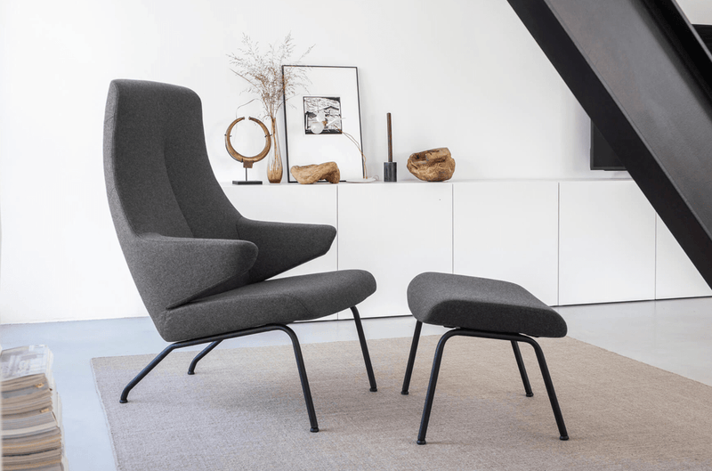 Sessel und Fußhocker VOOG mit dunkelgrauen Bezug und schwarzen Metallbeinen von Oot-Oot in einem modernen Wohnzimmer vor einem weißen Sideboard
