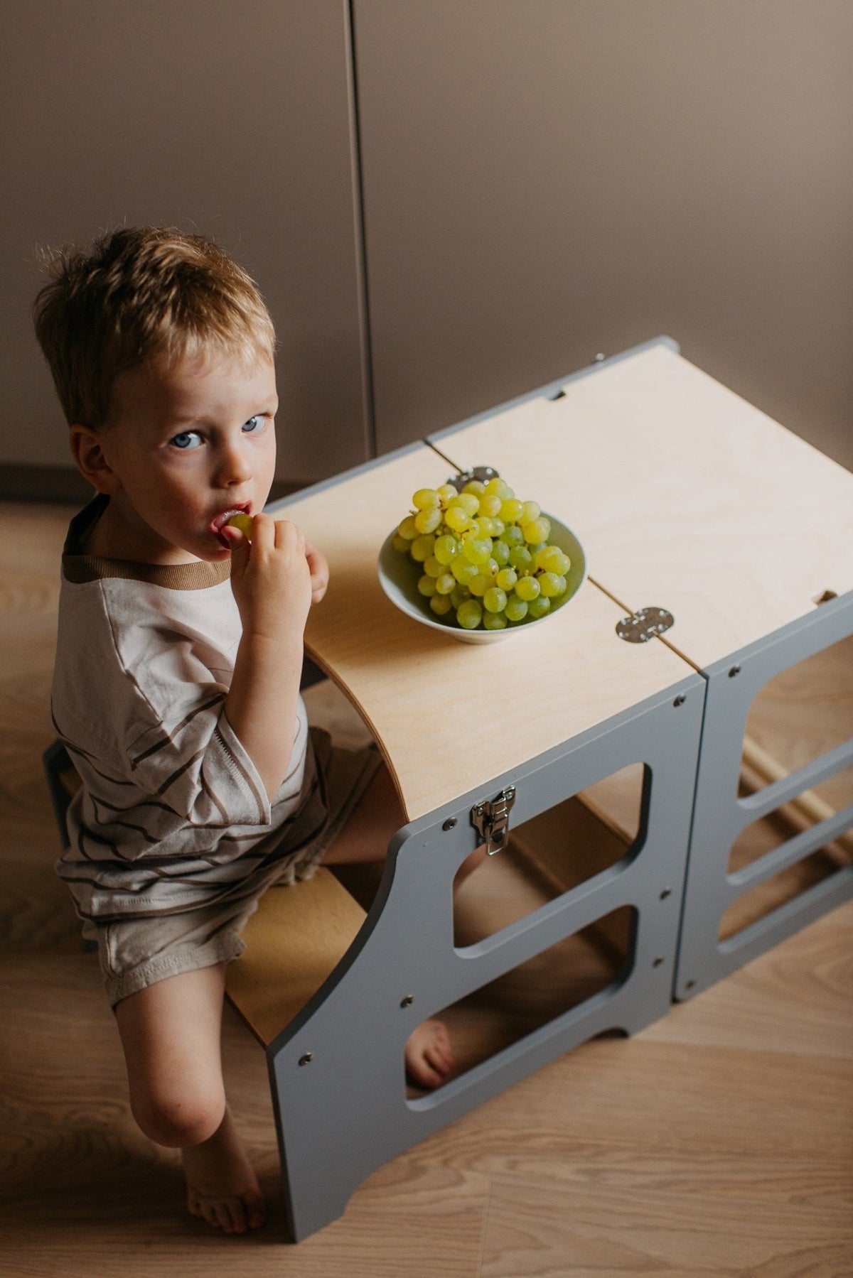 Junge sitzt am multifunktionalen 2-in-1 Lernturm & Kindertisch in skandinavischem Design in der Farbe grau, Hersteller: Duck Woodworks